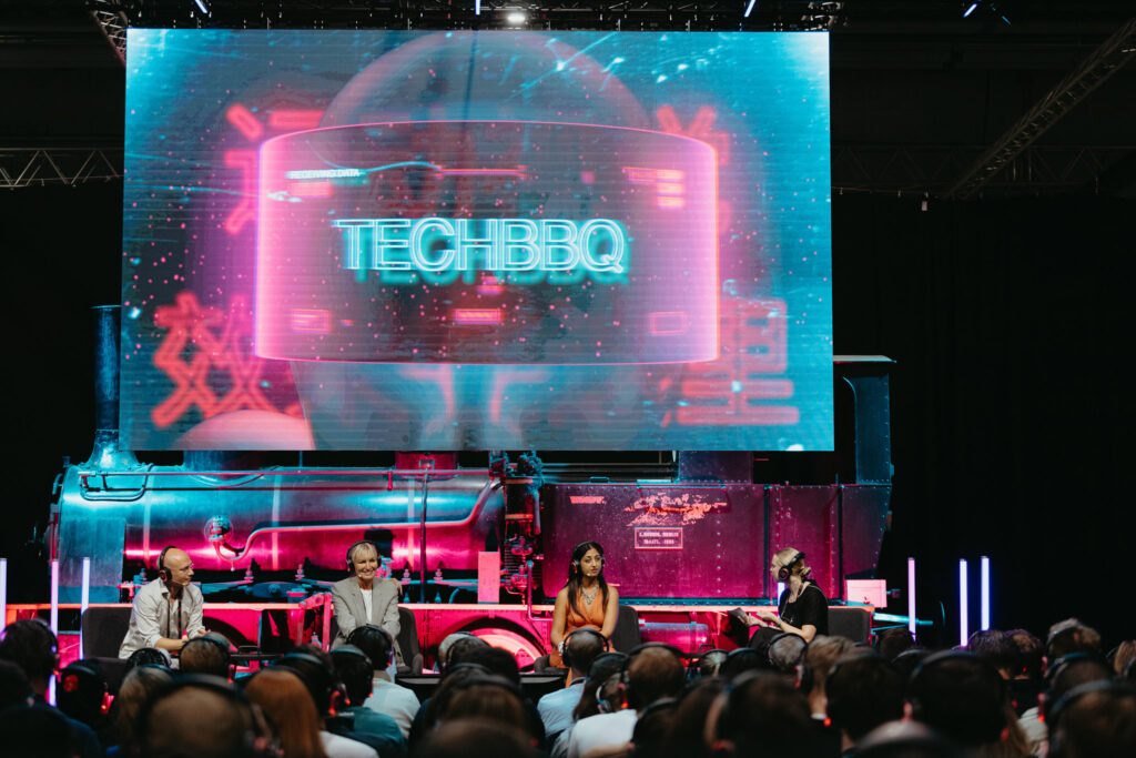Panel discussion with large “TechBBQ” digital screen in background.