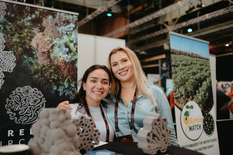 Two women at a TechBBQ booth showcasing eco-friendly technology.
