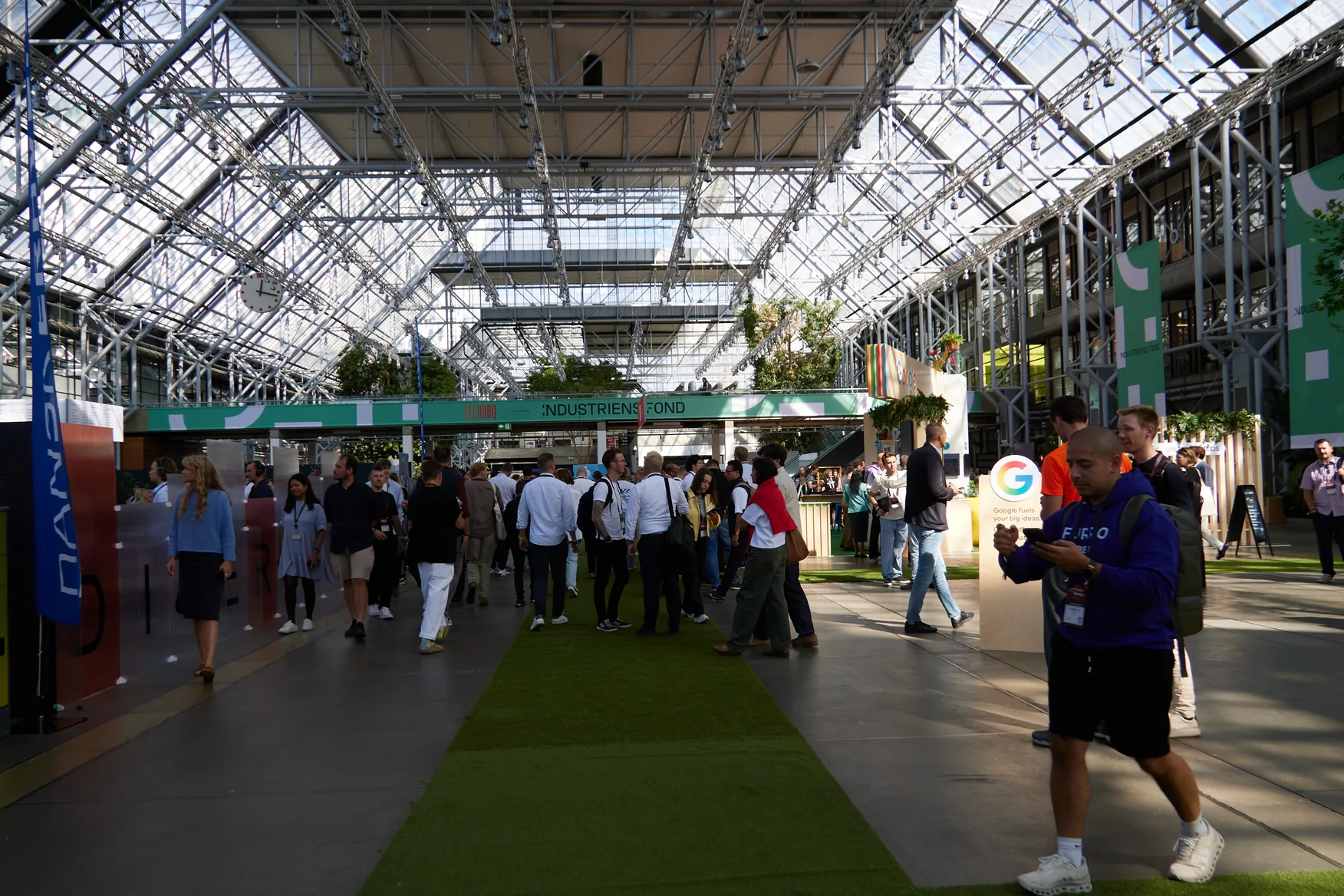 Attendees walking the green carpet aisle between exhibition stands at TechBBQ 2026