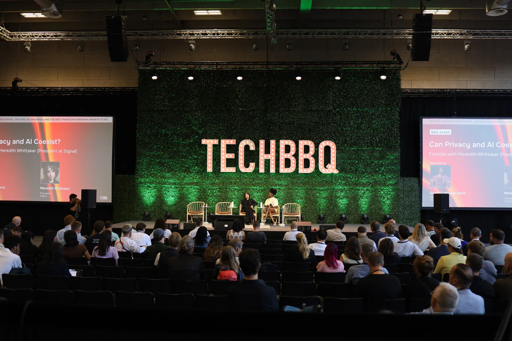 The TECHBBQ stage set against a green moss wall with the audience seated in front