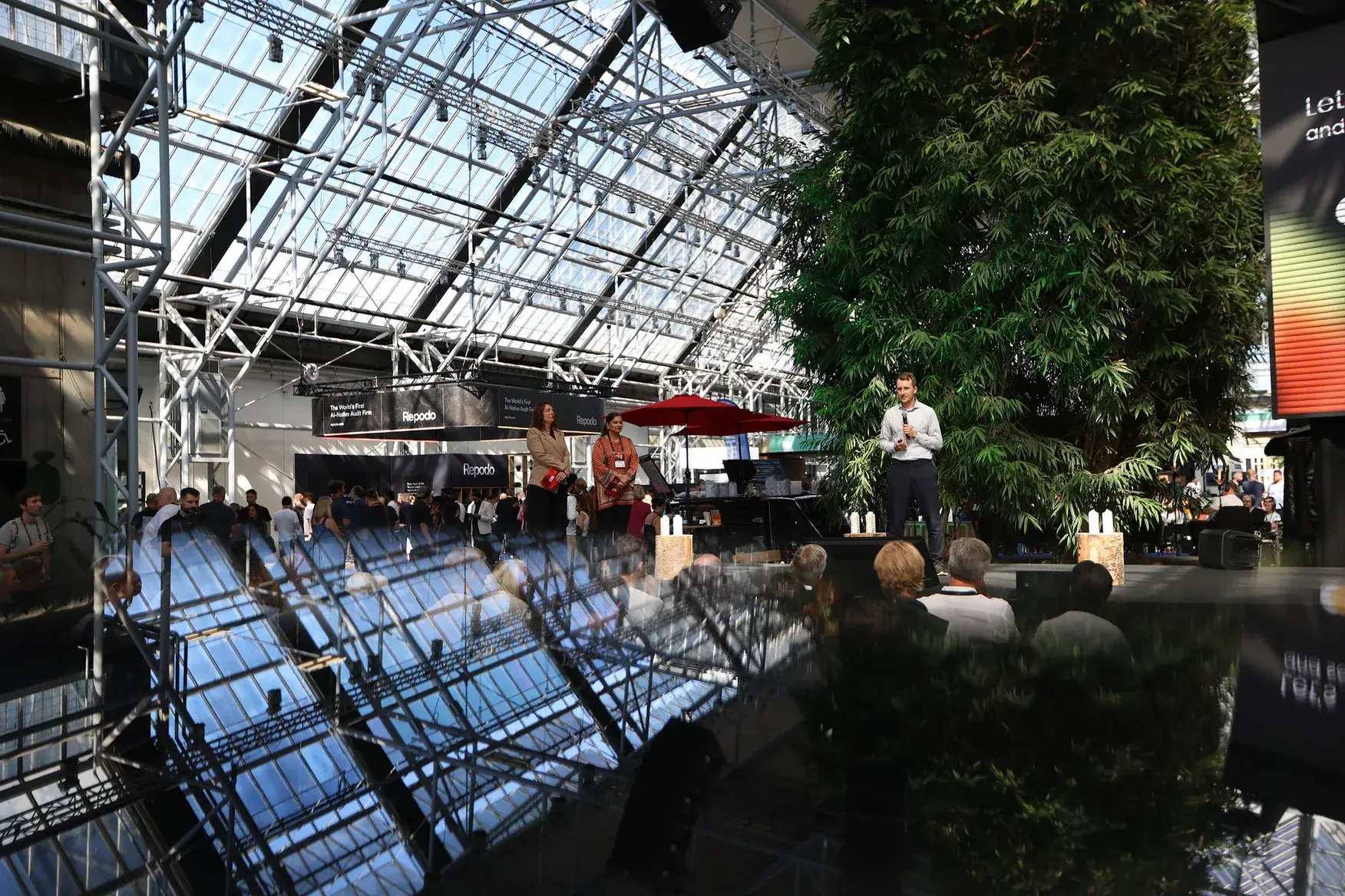 Bella Center hall with its glass roof and mature trees above the TechBBQ lounge area